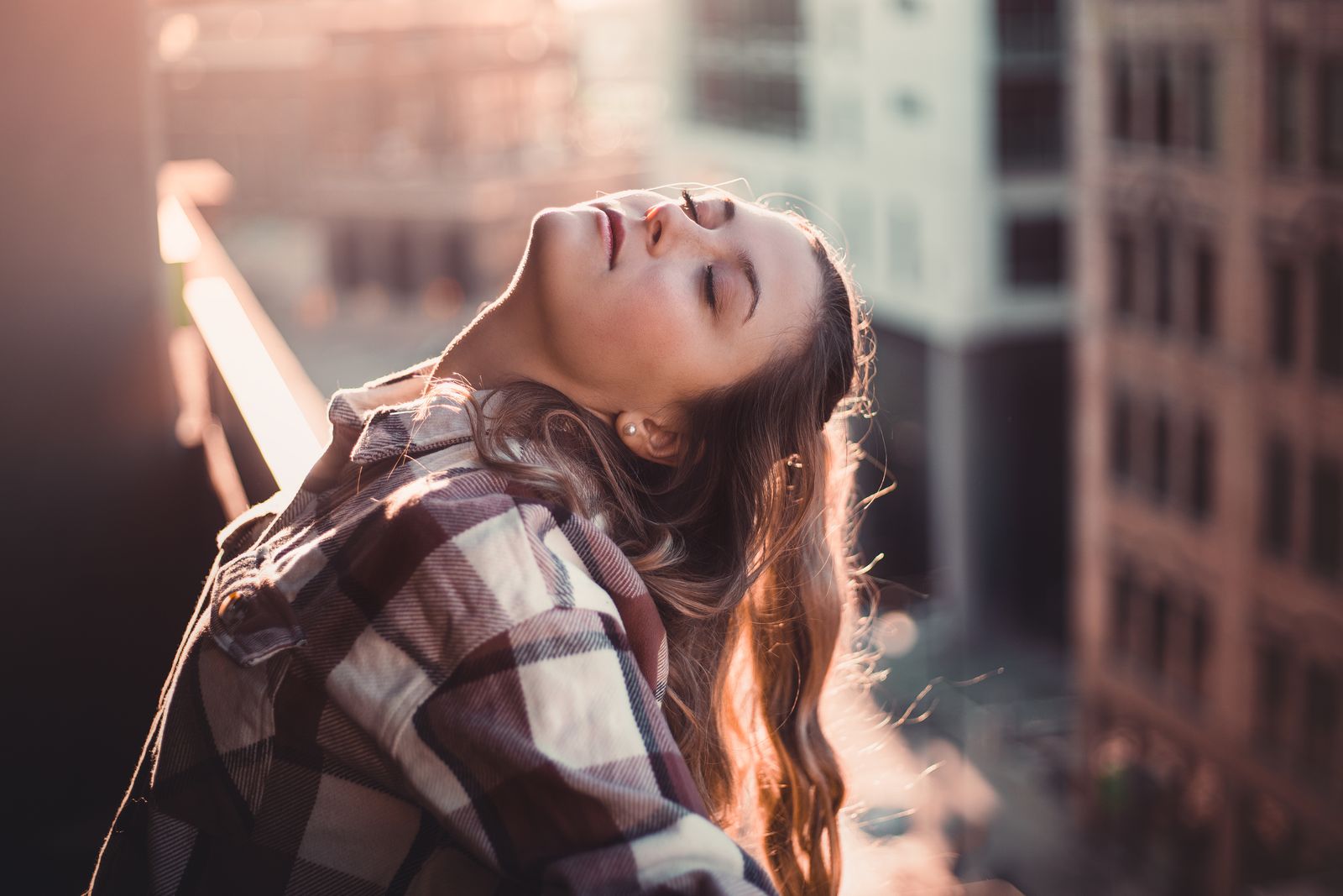 A peaceful moment captured as a woman closes her eyes, enjoying the sun on a city balcony.