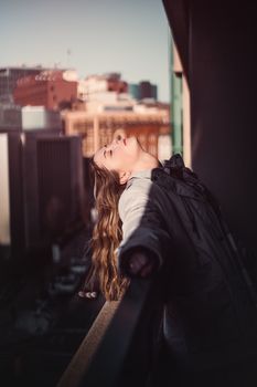 A woman leans back, eyes closed, enjoying a tranquil moment on a city balcony.
