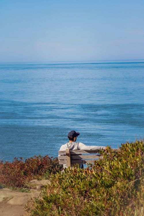 Free A man sits peacefully on a wooden bench, enjoying a tranquil seaside view. Stock Photo