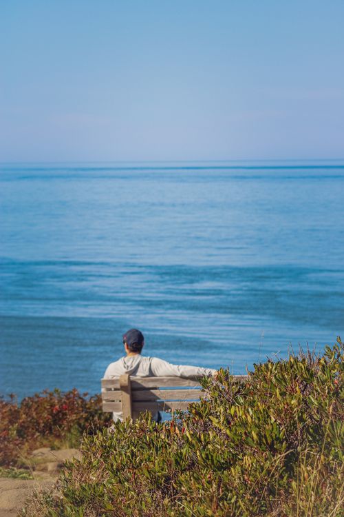 Free Man sitting on a bench enjoying a peaceful sea view. Perfect for relaxation themes. Stock Photo