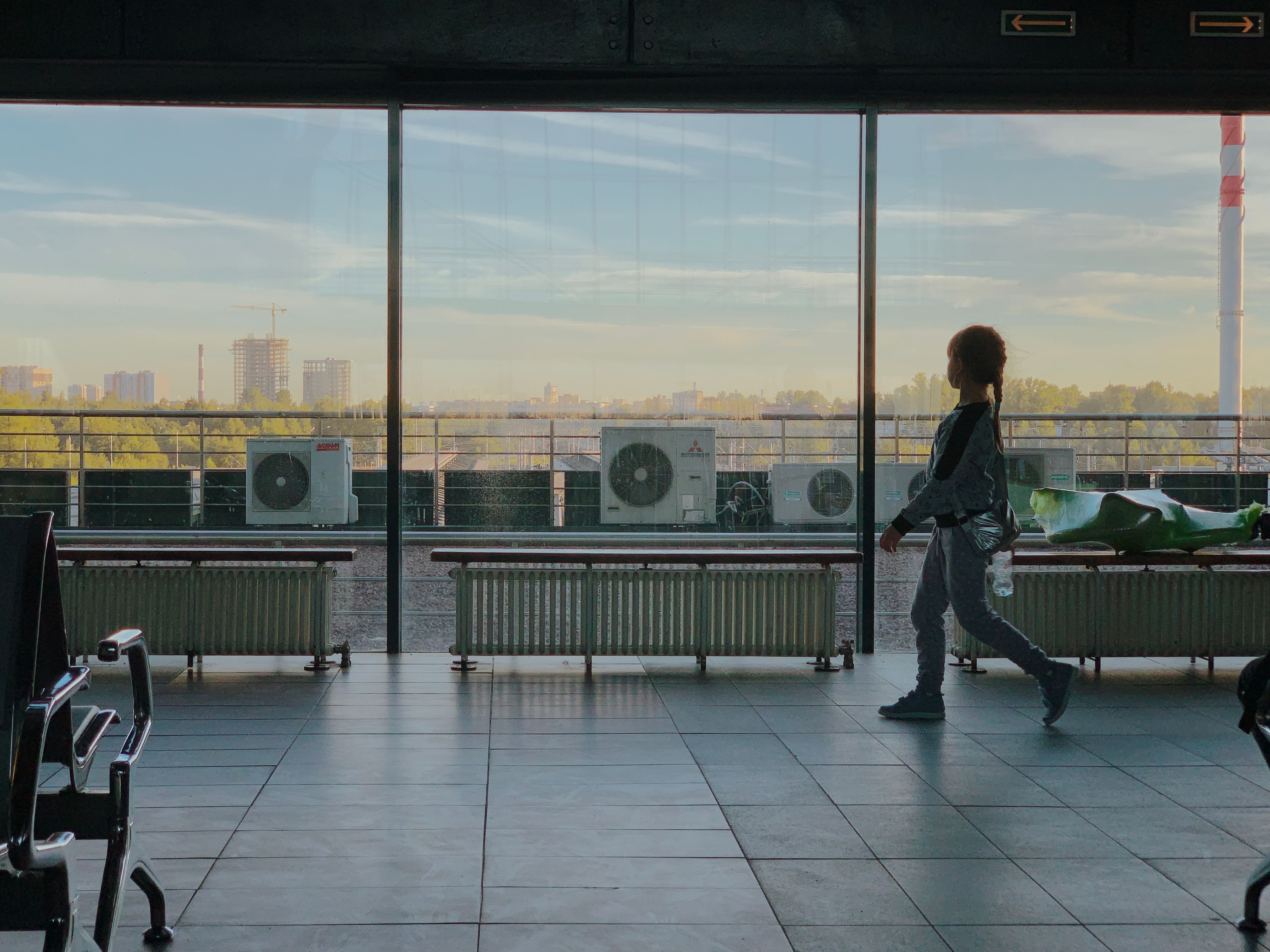 A child walking inside a modern airport terminal in Saint Petersburg, Russia, with a city view through large windows.