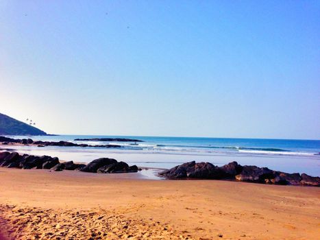 Peaceful beach scene with rocky shorelines, clear blue sky, and gentle waves.