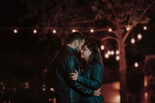 Free Couple in leather jackets embracing under string lights at night. Stock Photo