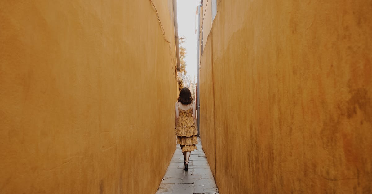 A woman in a yellow dress walks through a narrow alleyway with yellow walls in Hội An, Vietnam.