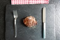 一块极简主义的扁平牛排，放在石板上，配着叉子和刀