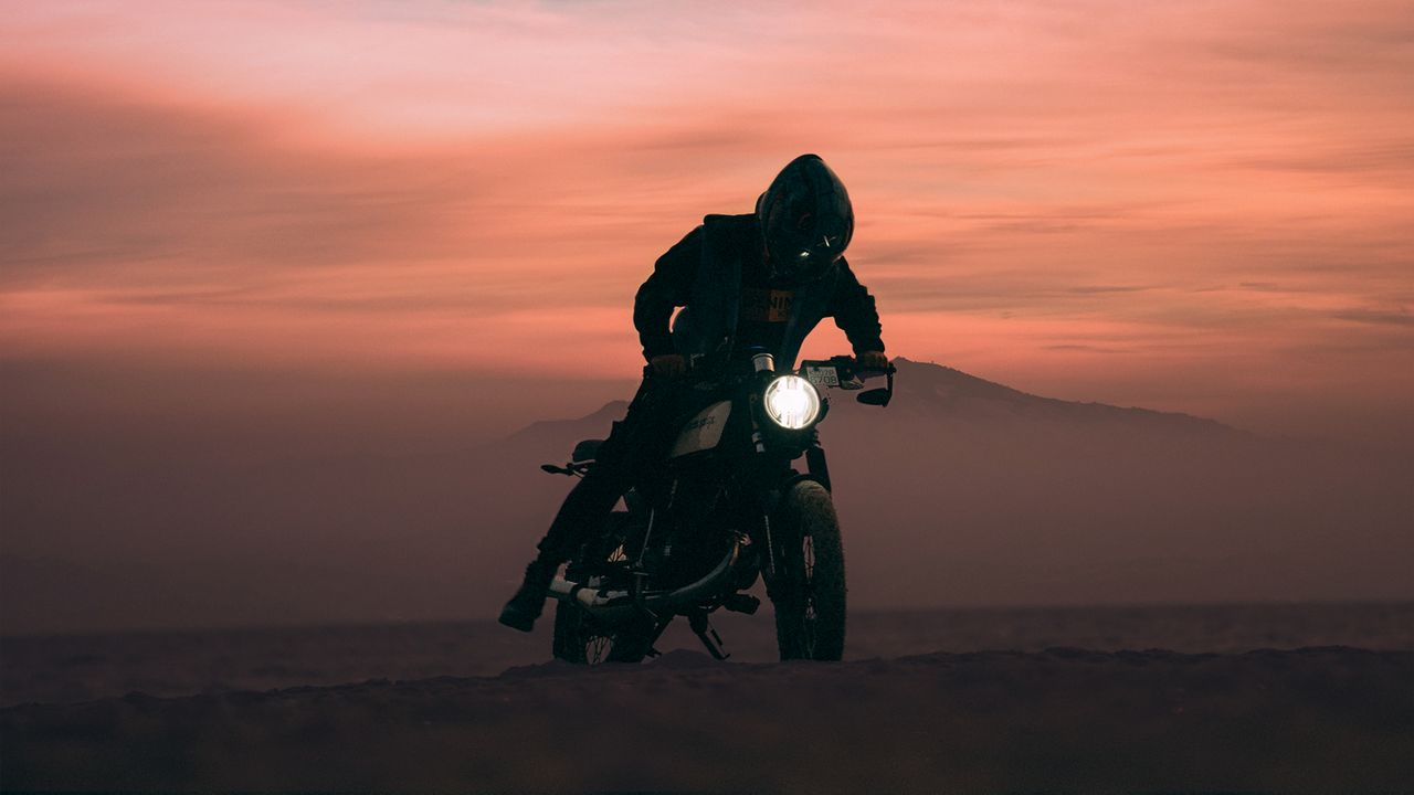 a motorcyclist rides through the desert at sunset creating a dramatic
