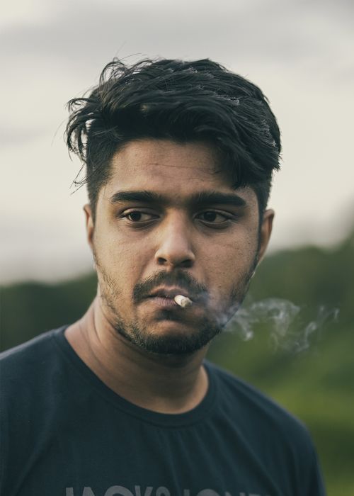 Free Close-up portrait of a young man smoking a cigarette outdoors, expressing thoughtful mood. Stock Photo
