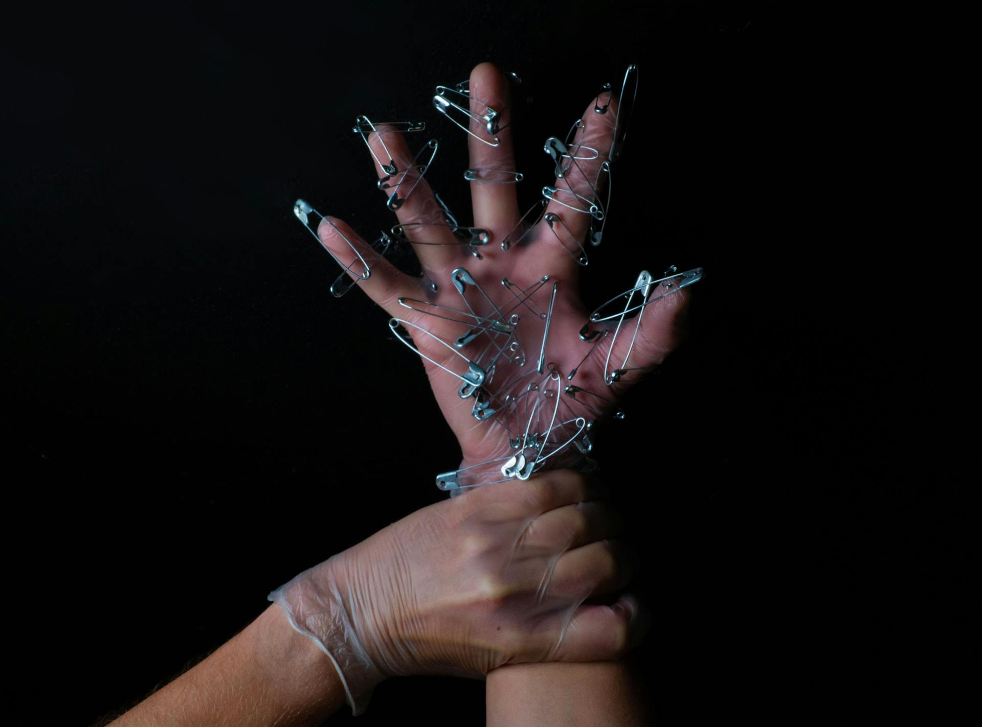 A hand covered with safety pins held by another hand, symbolizing protection and restraint.