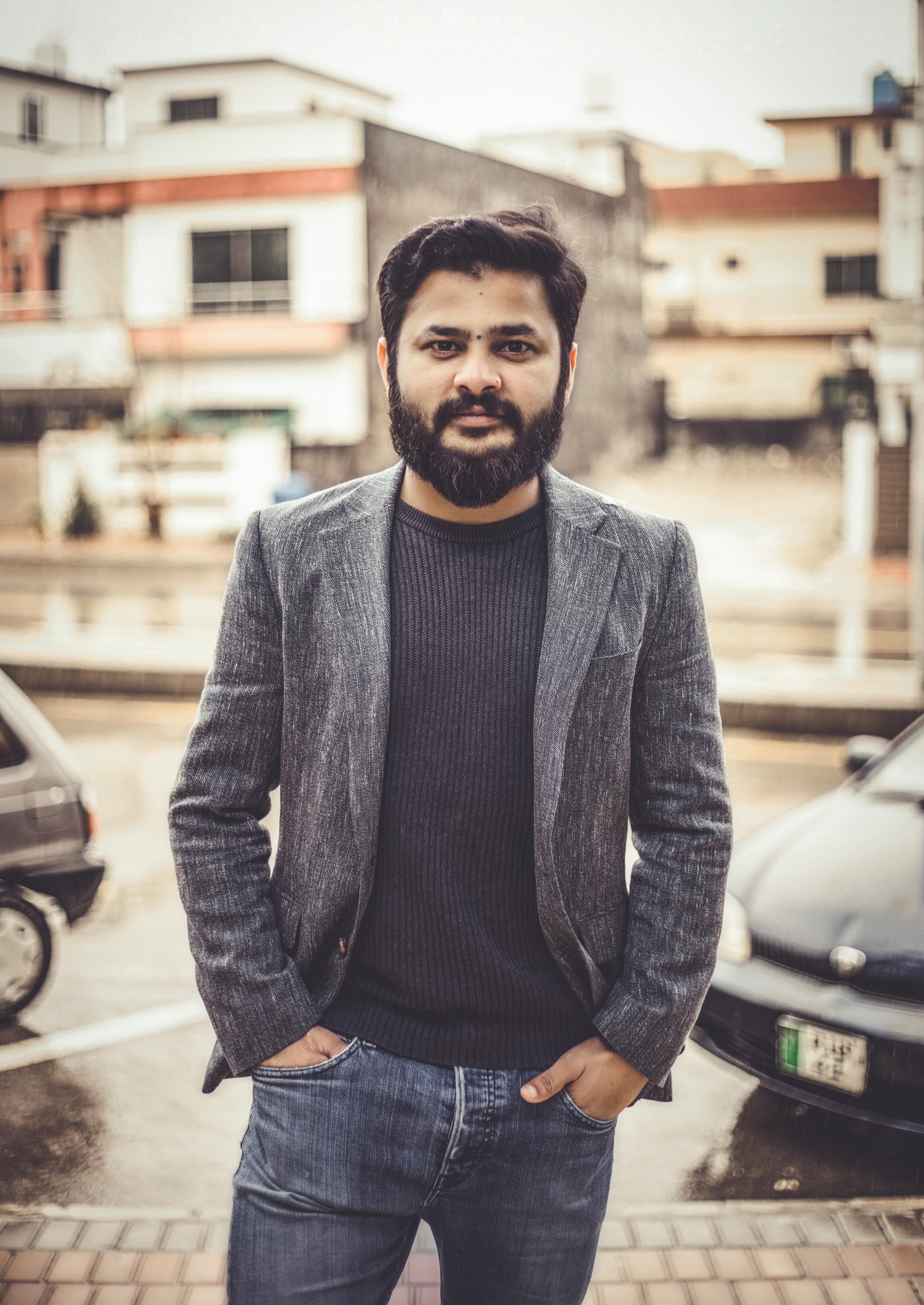 A bearded man in a blazer poses confidently outdoors in an urban setting, Islamabad.