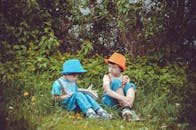 两个男孩戴着五颜六色的帽子，坐在郁郁葱葱的花园草地上一起阅读