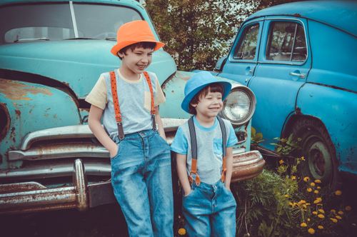 Free Two smiling boys in stylish suspenders beside vintage cars on a sunny day outdoors. Stock Photo