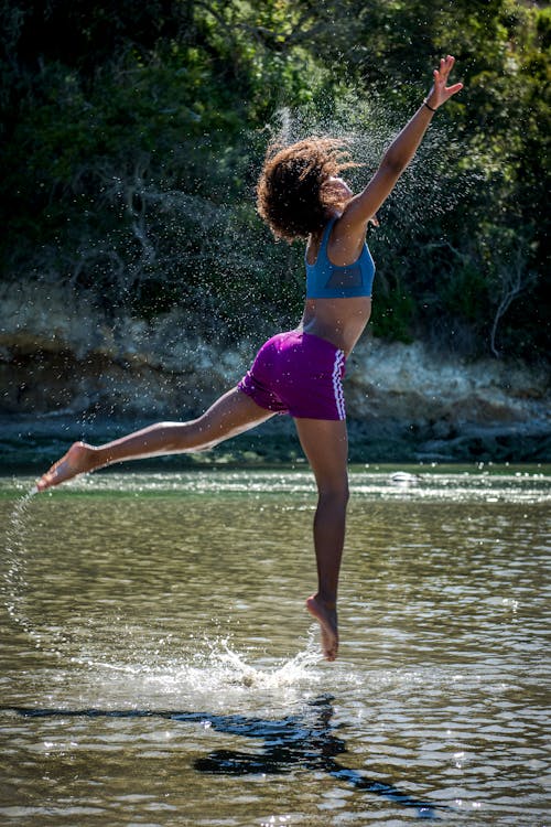 Женщина в синем спортивном бюстгальтере и фиолетовых шортах прыгает над водой
