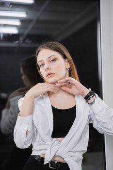 Young woman posing confidently indoors with fashionable attire in front of a mirror.