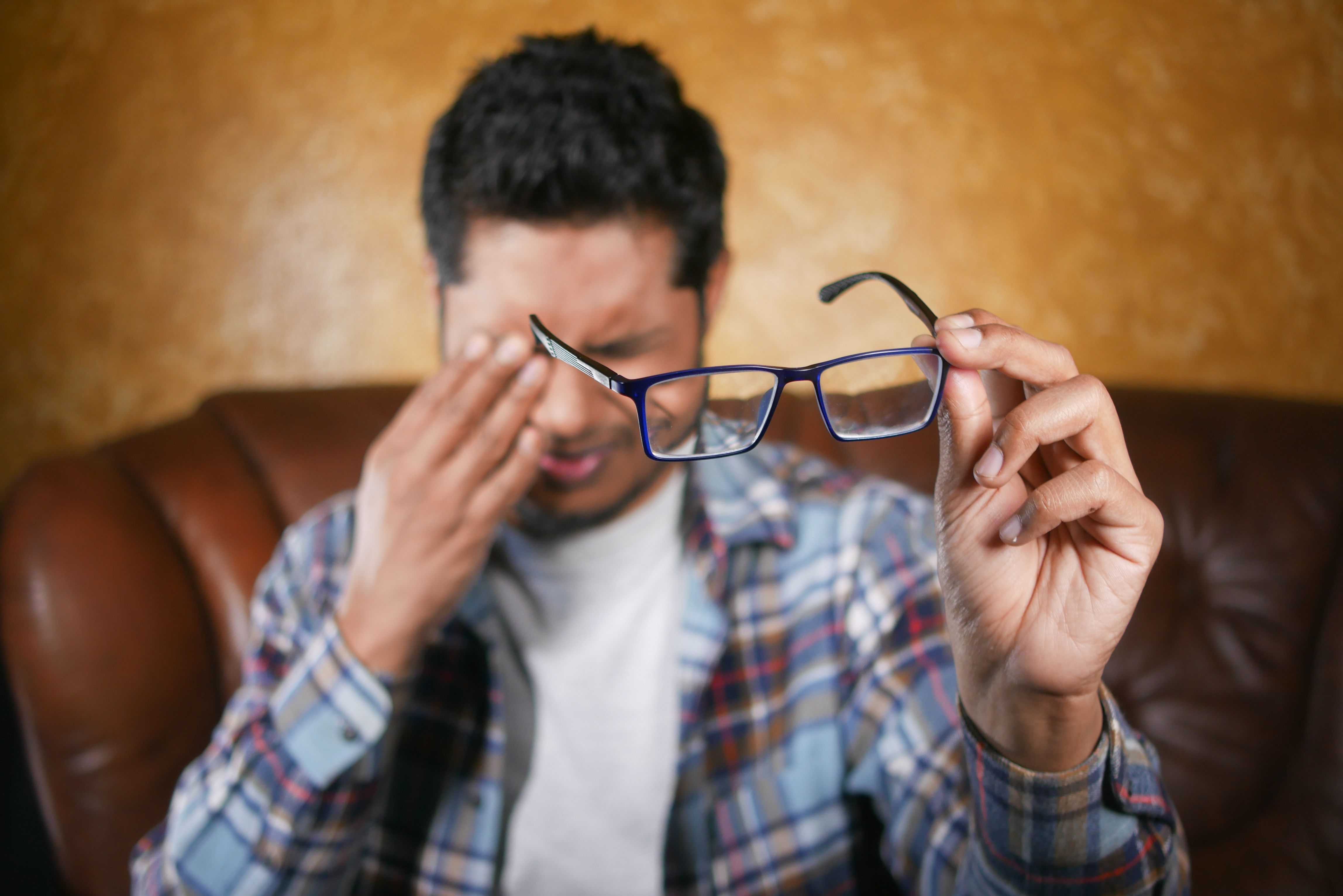 A man in plaid shirt holding eyeglasses indoors. Focus on eyewear with neutral background. - remove scratches from glasses