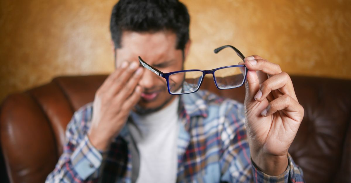 Remove Scratches from Glasses: 8 Products That Actually Work 1 A man in plaid shirt holding eyeglasses indoors. Focus on eyewear with neutral background. - remove scratches from glasses
