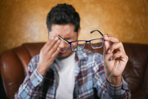 Free A man in plaid shirt holding eyeglasses indoors. Focus on eyewear with neutral background. Stock Photo
