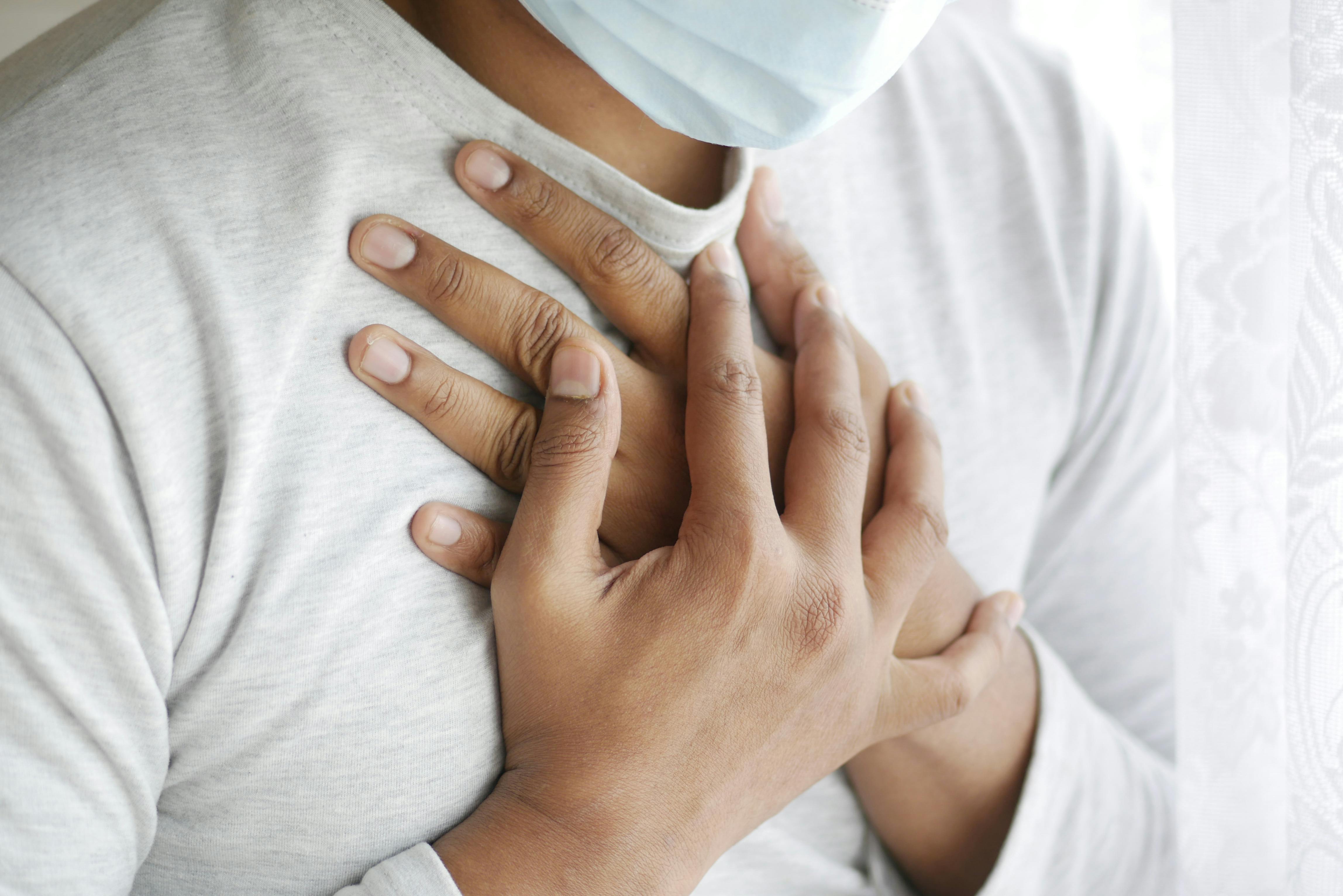 Close-up image of a masked person holding chest, symbolizing health concerns.