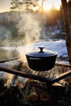 Cast iron pot steaming on a grill outdoors during sunset in winter.