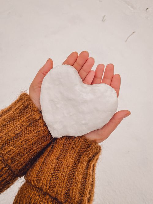 Free Hands in cozy sweater holding a snow heart, symbolizing love and warmth in winter. Stock Photo