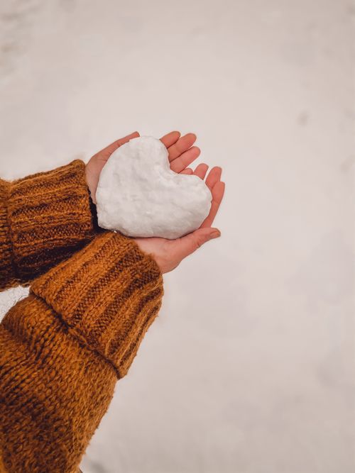 Free Close-up of hands holding a heart-shaped snow piece, symbolizing love in winter. Stock Photo
