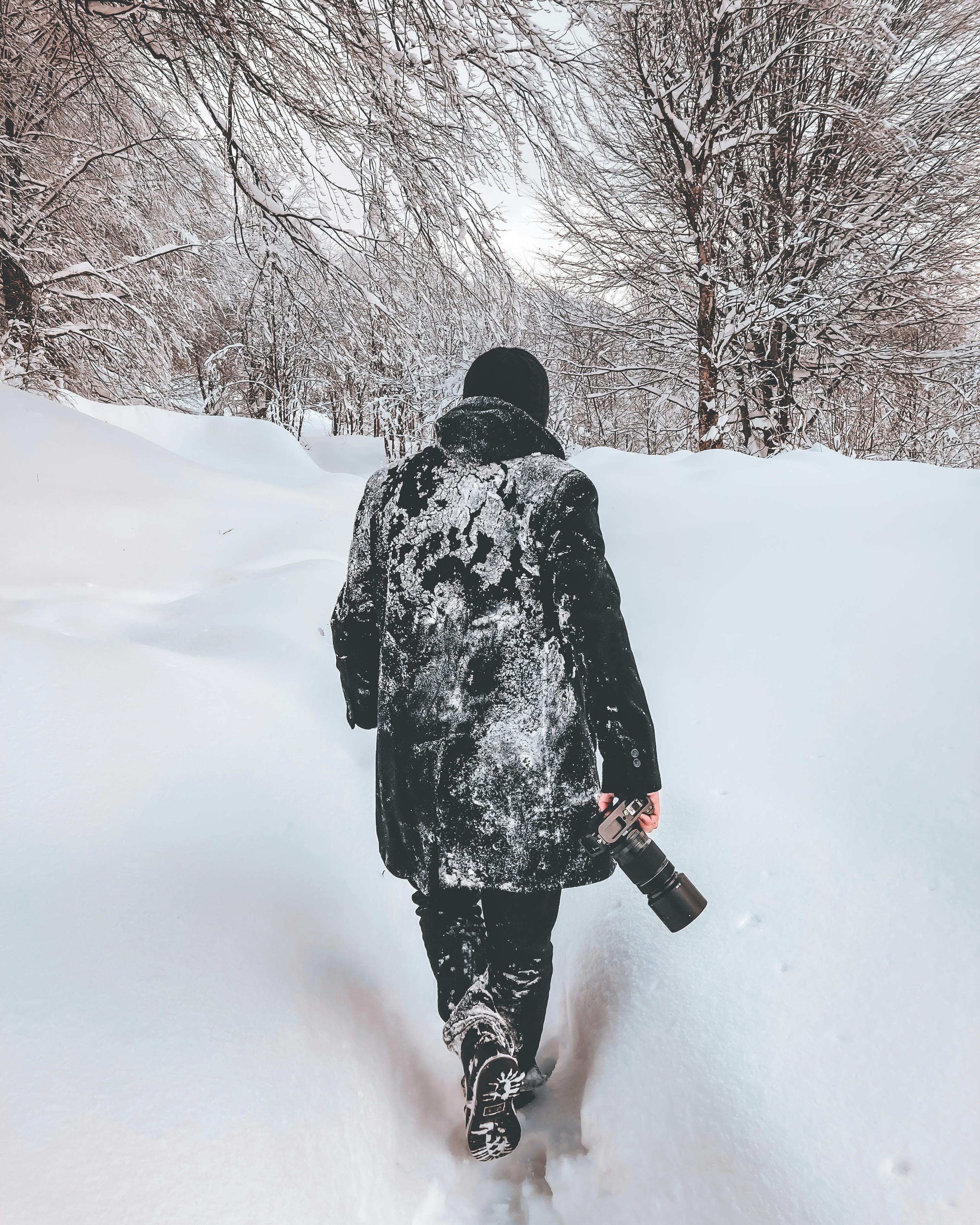A person walks through a dense, snow-covered forest in winter, holding a camera.