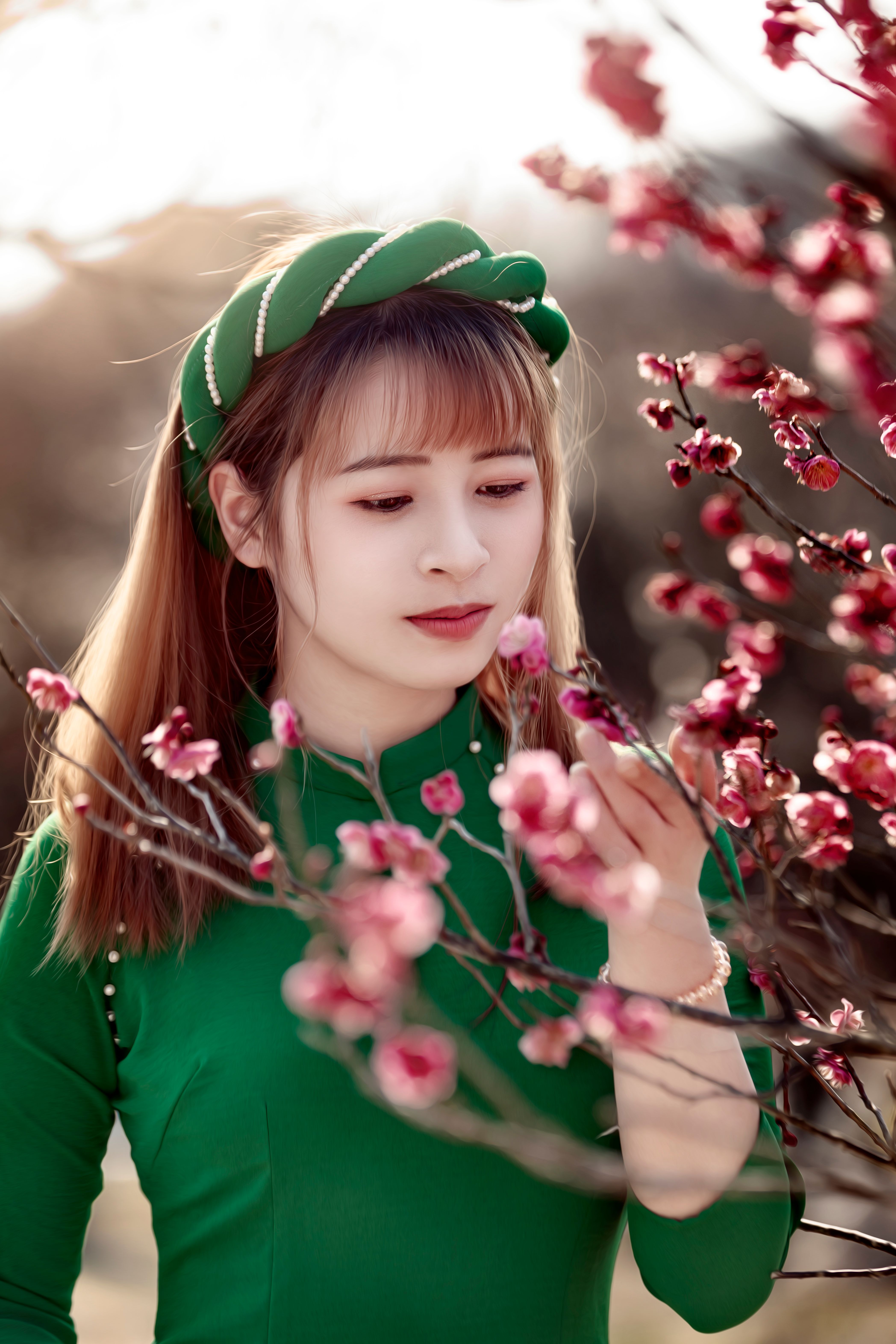A young woman in green admires pink blossoms on a sunny spring day.