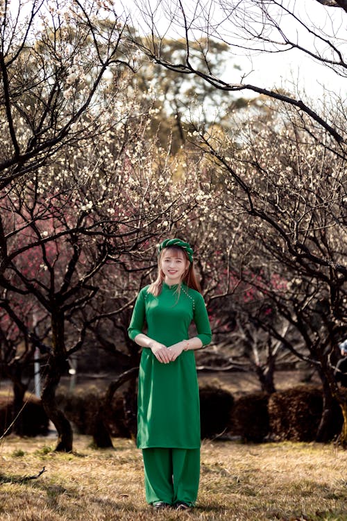 Free Woman in Green Dress Standing Near Leafless Trees Stock Photo