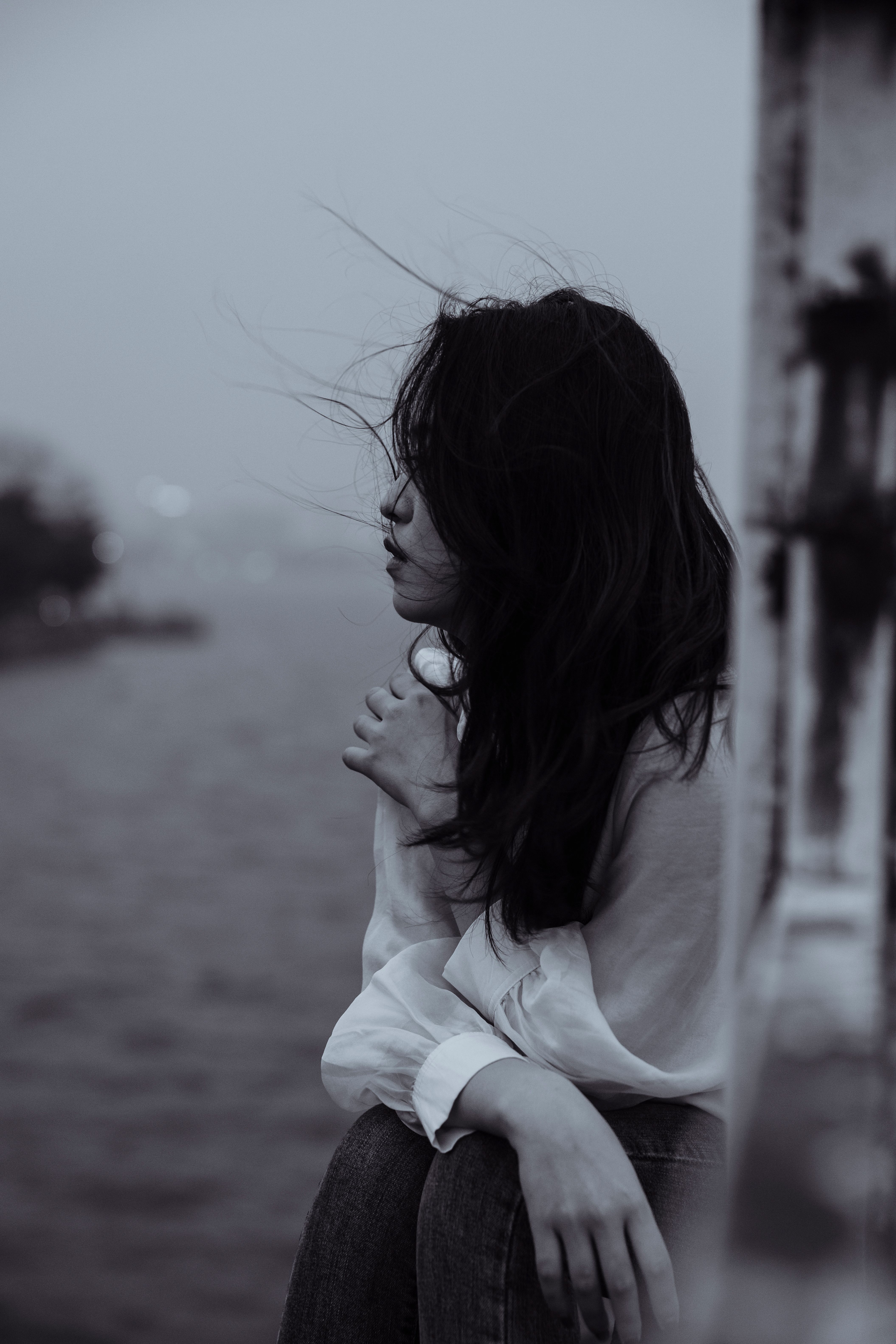 A thoughtful woman in black and white, sitting by a river, exuding a sense of calm and introspection.