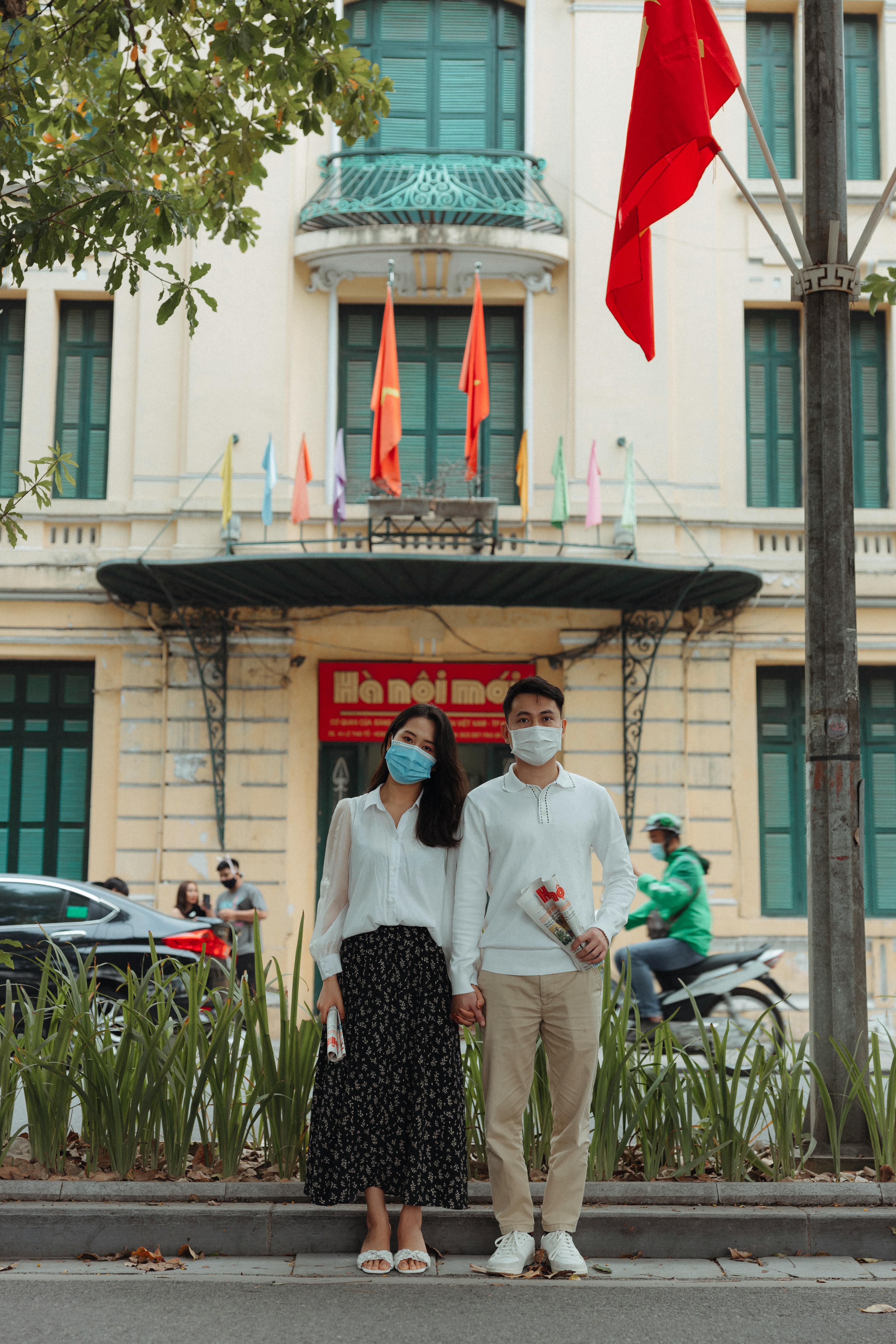 Asian couple wearing masks holding hands on a city street, symbolizing love during the pandemic.