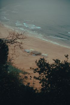 A peaceful view of a sandy beach with gentle waves and beachfront buildings on a moody day.
