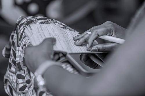 Grayscale Photo of Person Holding a Paper and Pen