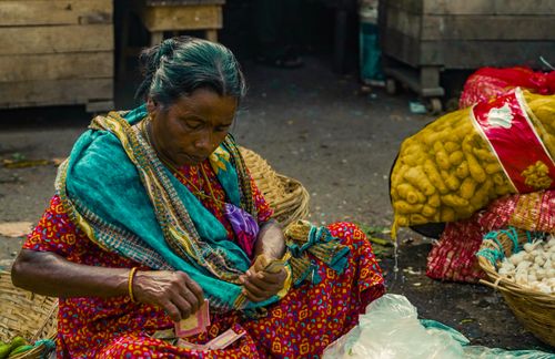 Free Senior woman in traditional clothing selling vegetables at a bustling market in Dhaka, Bangladesh. Stock Photo