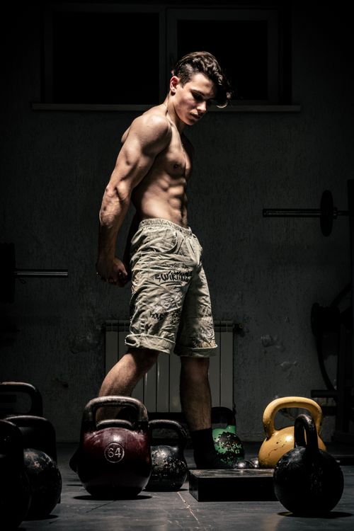 Free Athletic man flexing near kettlebells in moody gym lighting. Stock Photo