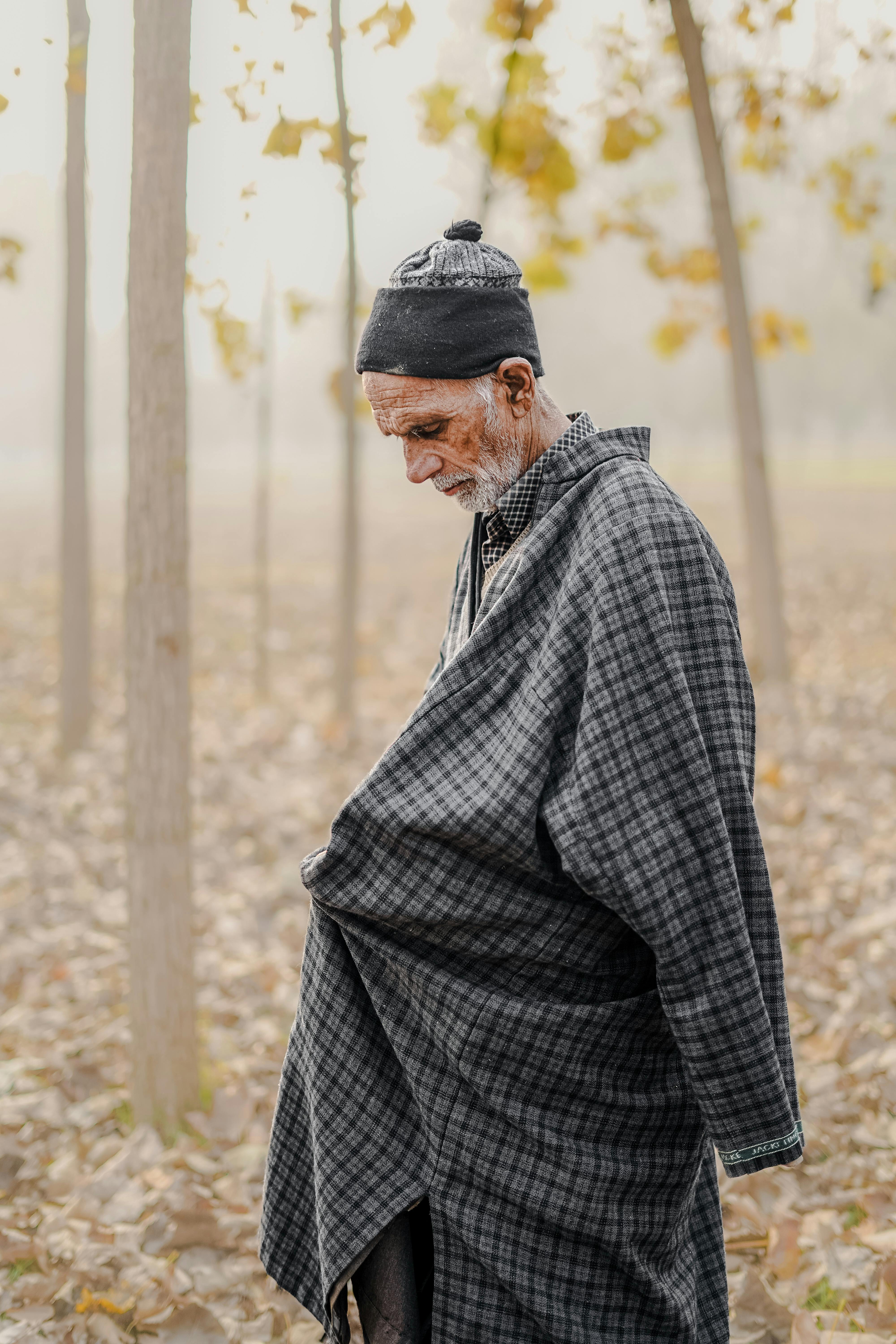 Elderly man in plaid clothing looking down thoughtfully in an autumn forest setting.