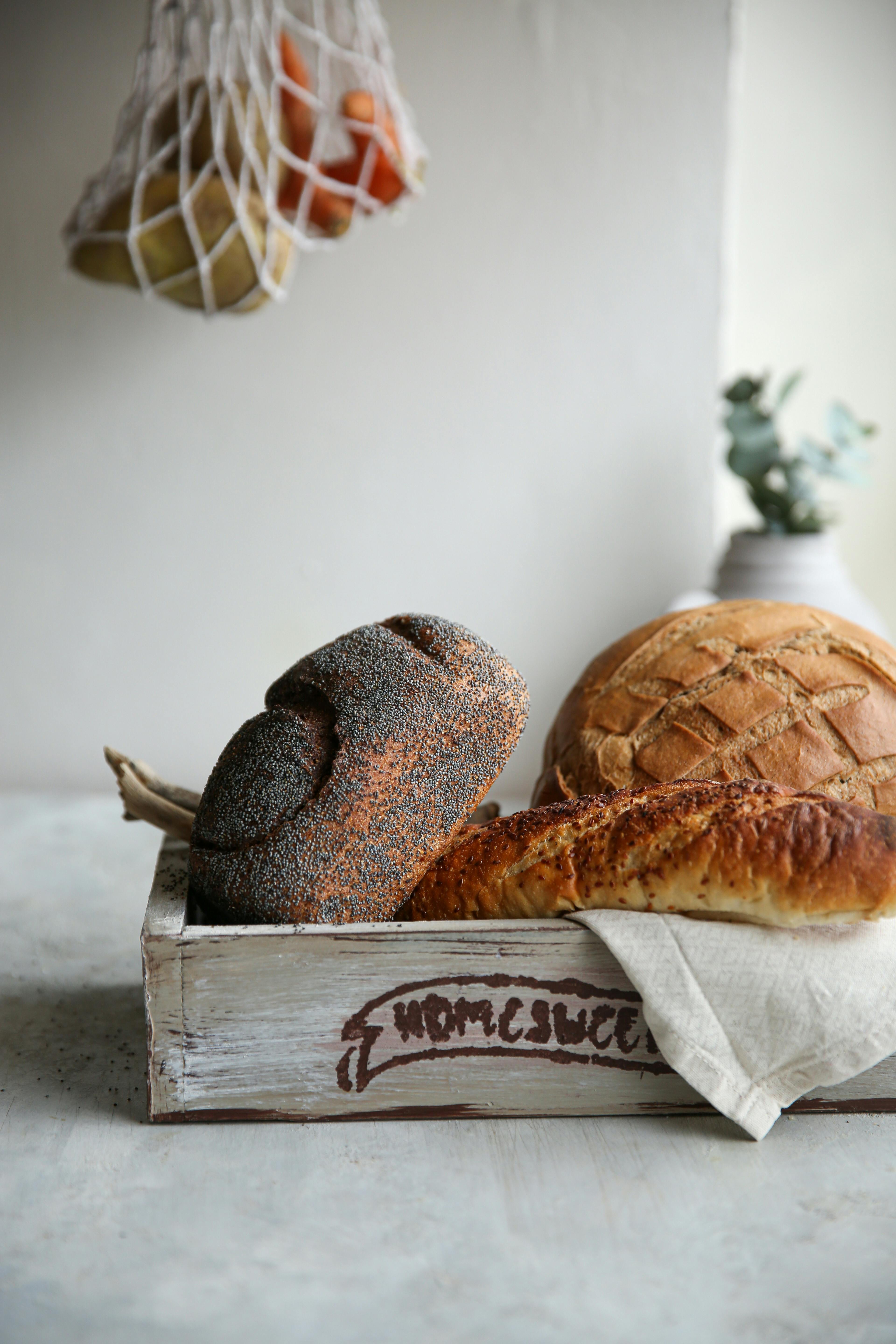 Variety of fresh breads in a wooden crate placed on a light surface.
