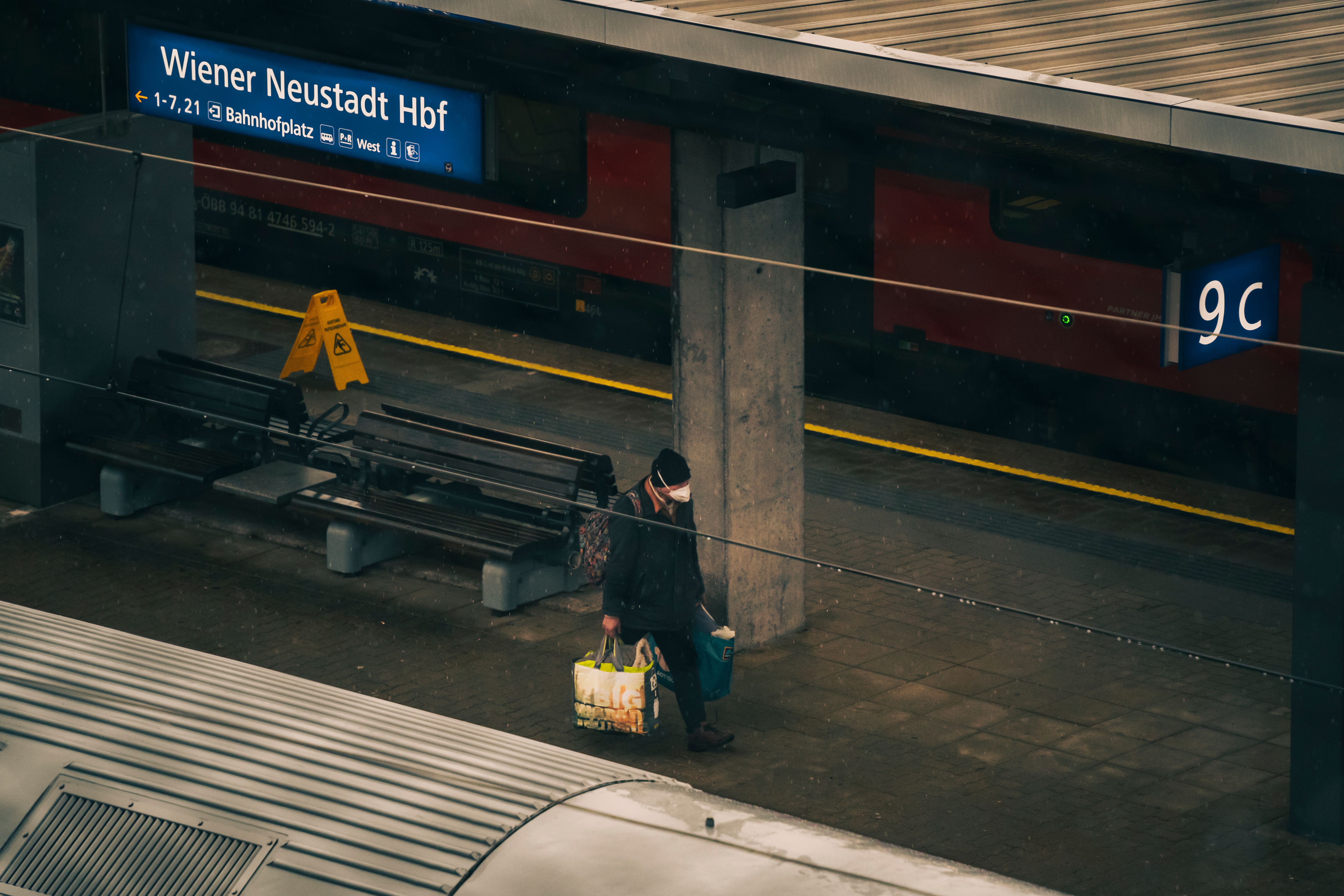 Man wearing a face mask carrying bags at Wiener Neustadt train station in winter.