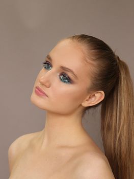 Portrait of a woman with striking eye makeup and ponytail in a studio setting, showcasing elegance and modern beauty.