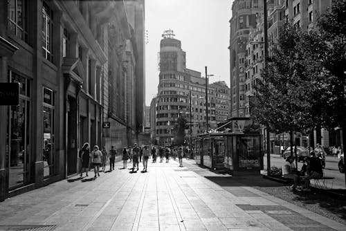 Grayscale Photo of People Walking on City Street near Buildings