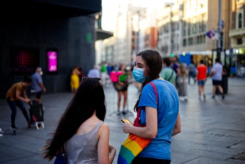 Free A vibrant urban street scene in Madrid featuring people wearing masks and a rainbow flag. Stock Photo