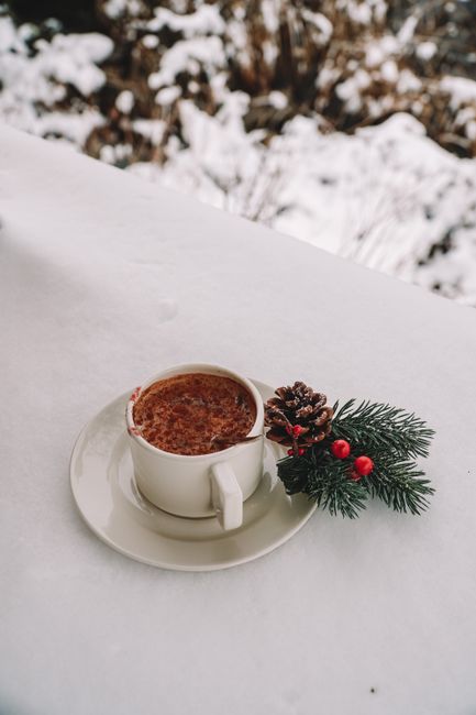 Warm coffee cup on snow with festive pine decor, perfect for winter and holiday themes.