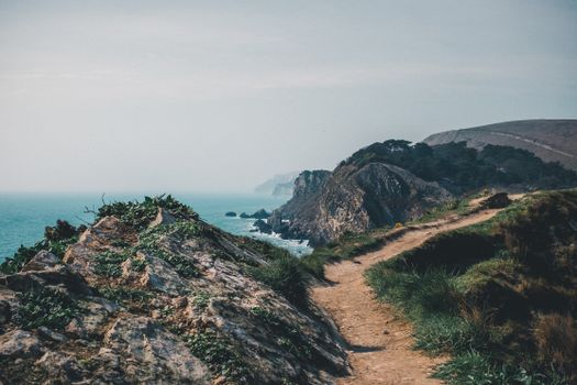 Discover the beauty of a coastal path winding through rocky cliffs with an expansive ocean view.