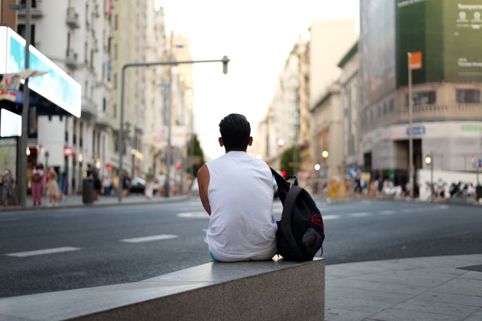 Vista trasera de un hombre sentado en un banco de la calle en Madrid, capturando la soledad urbana.