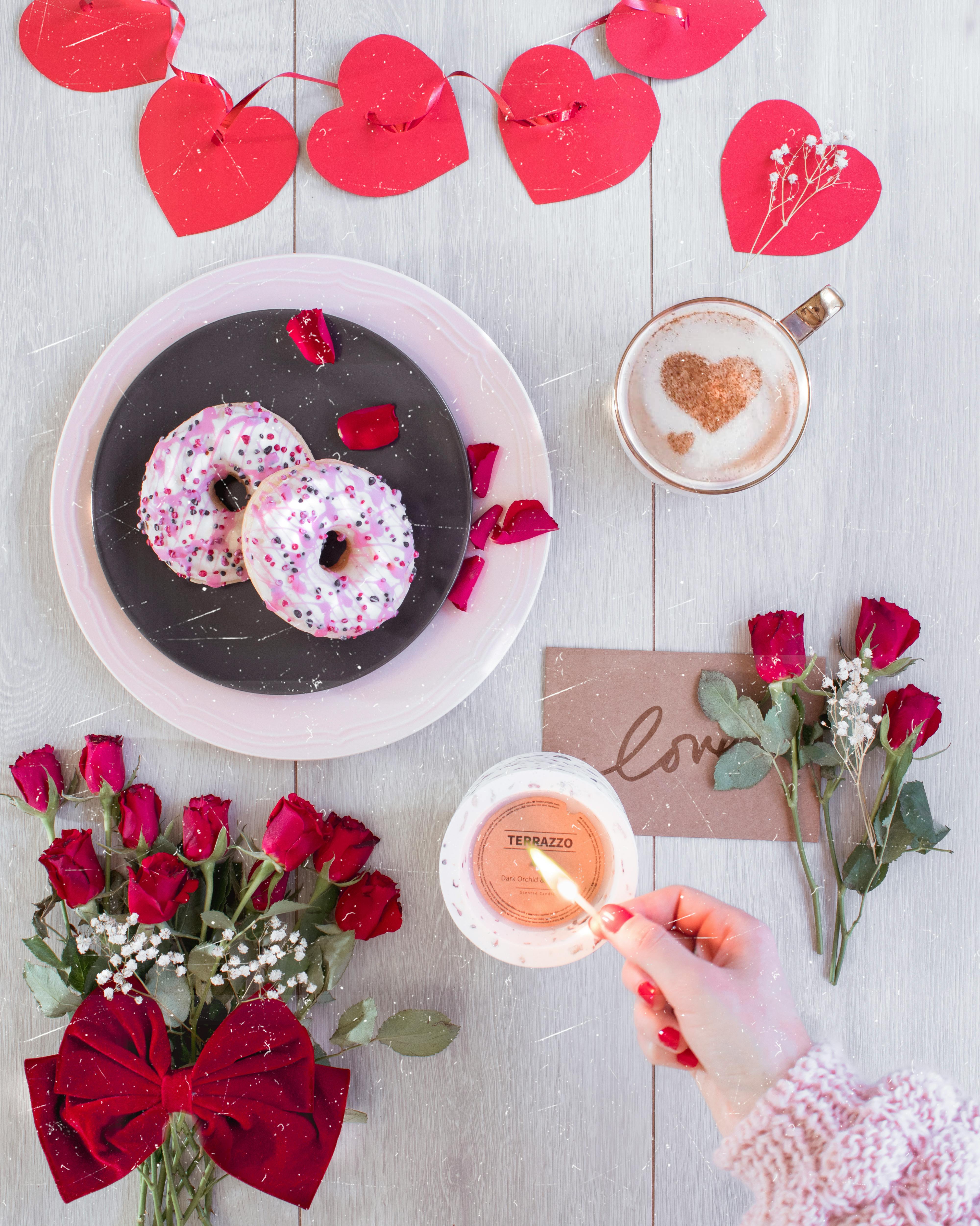 Top view of Valentine's donuts, roses, and a heart coffee on a light wooden table, capturing love's essence.