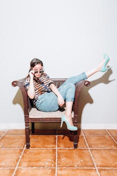 Stylish teenage girl in sunglasses and heels lounging on a chair indoors.
