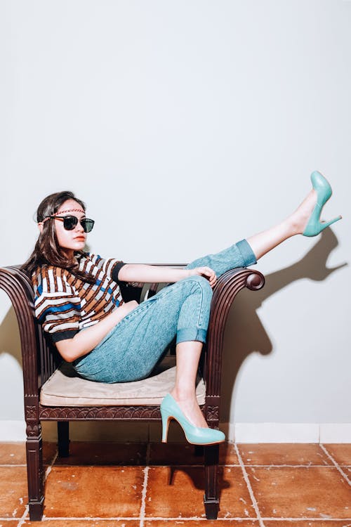 Free Woman in Blue Denim Jeans and Black Sunglasses Sitting on Brown Wooden Chair Stock Photo