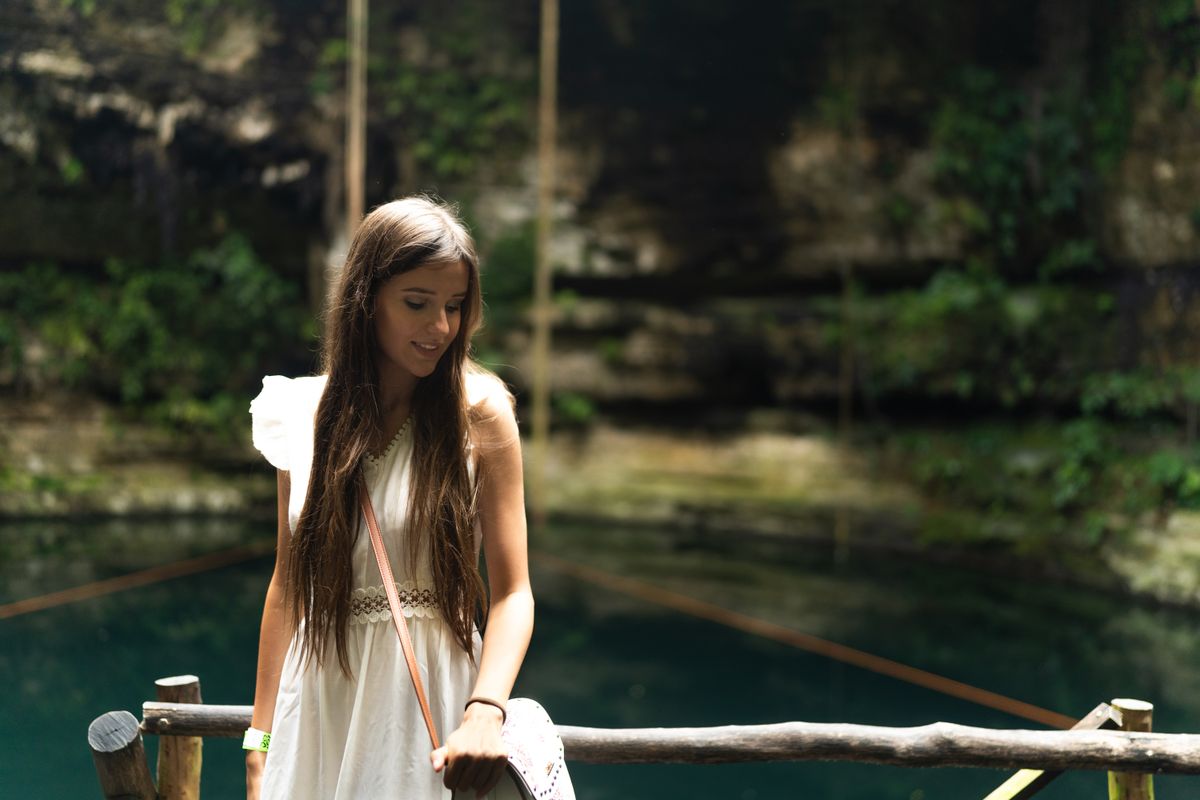 Una mujer en vestido blanco está de pie junto a un cenote en Playa del Carmen, México.