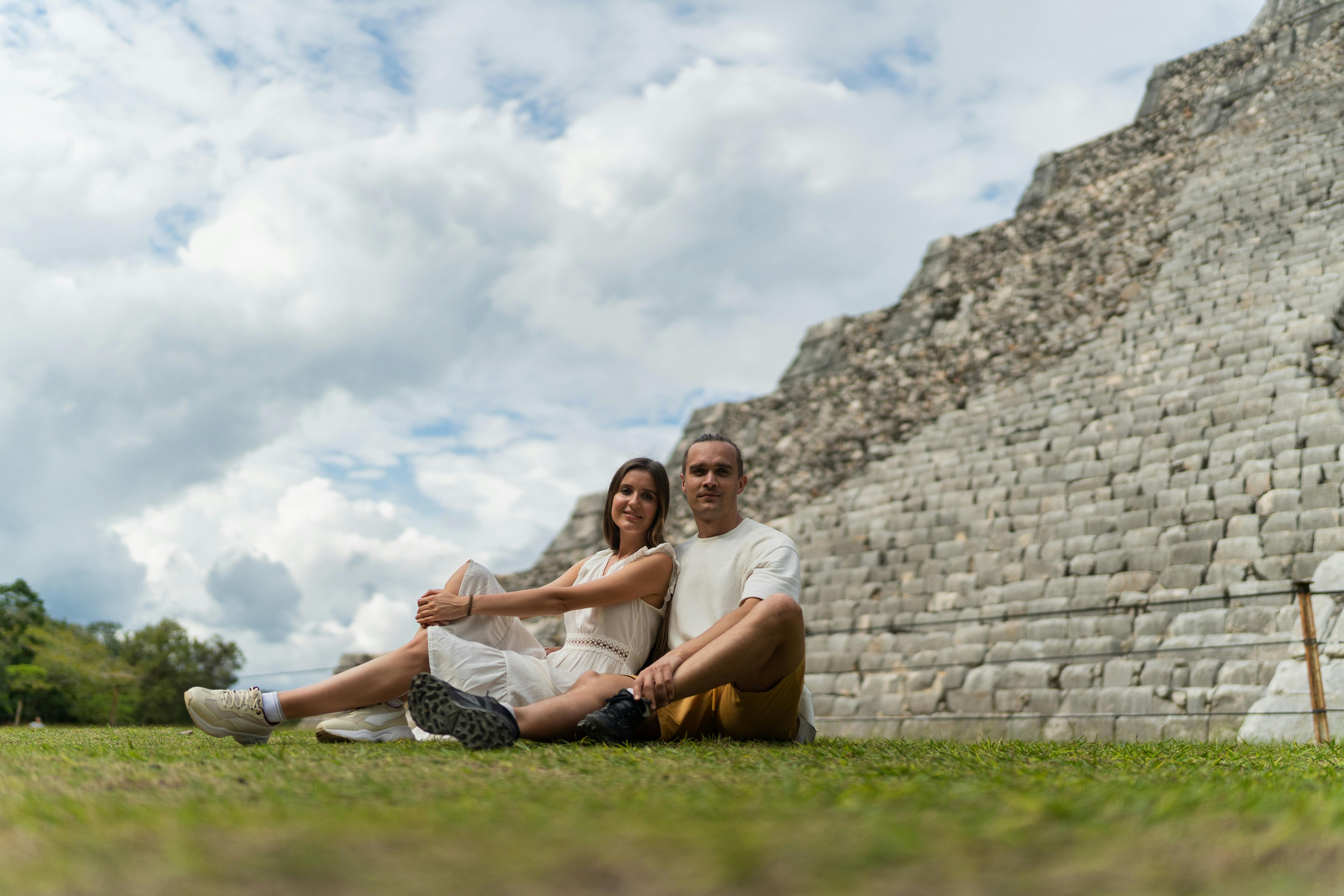 authentic mayan cultural experiences mexico - Happy couple sitting near ancient Mayan pyramid in Yucatan, enjoying a sunny day outdoors.