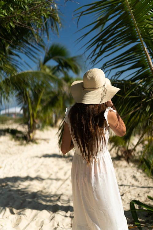 Woman Wearing Sun Hat in White Dress Standing on White Sand