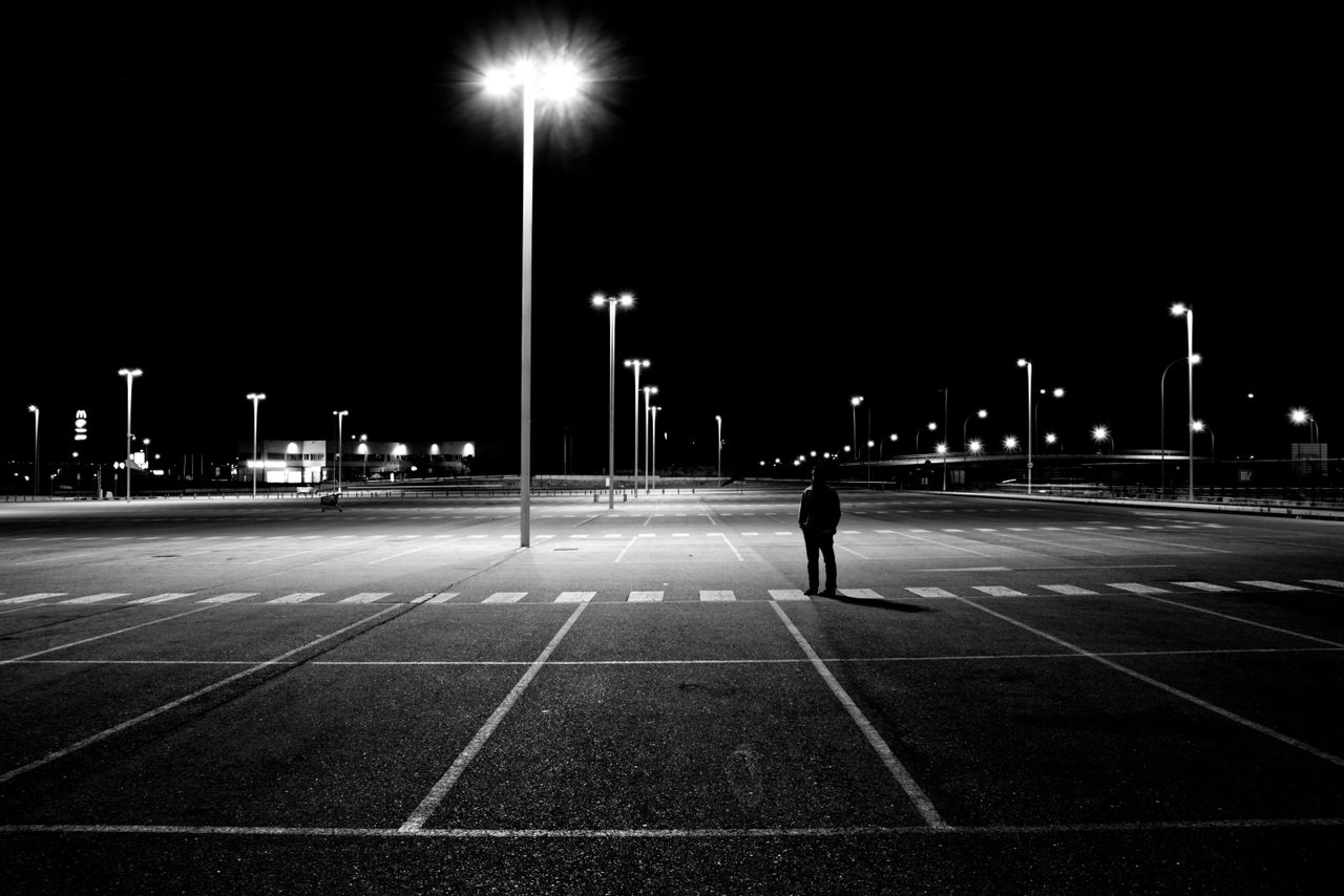 a solitary figure stands in an illuminated parking lot at night creati