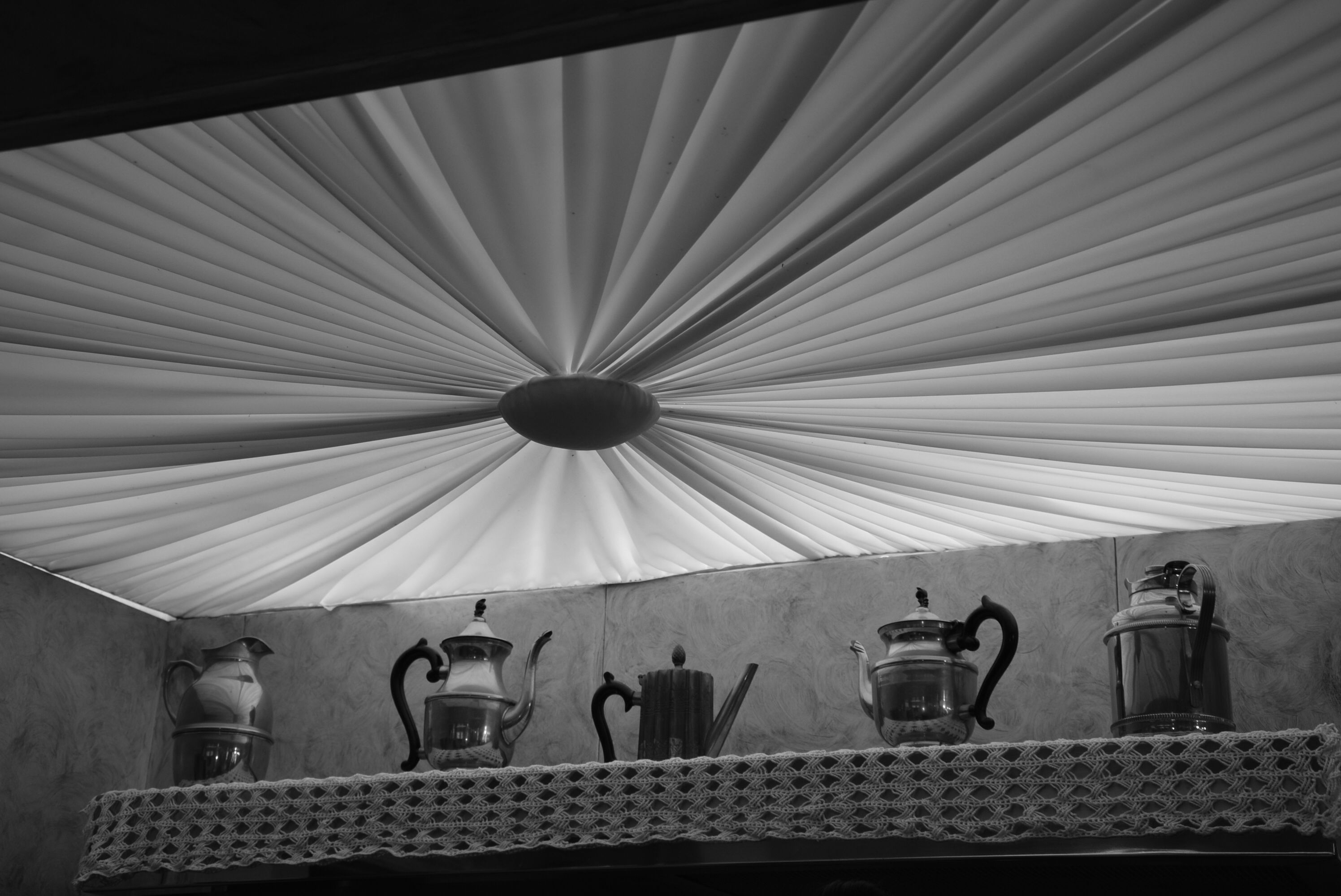 Black and white photo of vintage kettles under a decorative ceiling.
